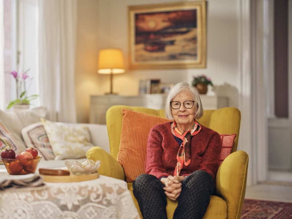 A smiling client sits in her armchair at home