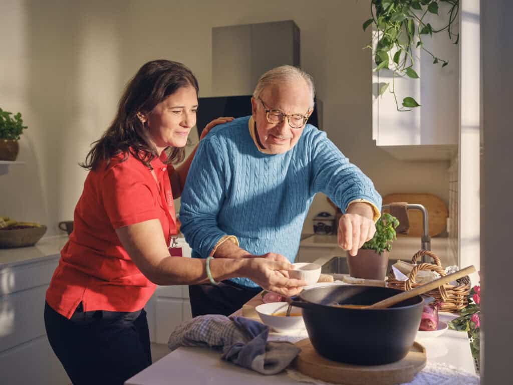 Older man and caregiver preparing a meal together, illustrating the benefits of Personal Care assistance. 