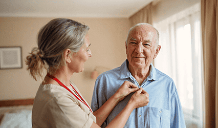 Caregiver helps client living with arthritis to button his shirt