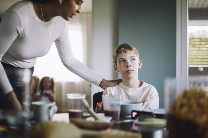 Mother consoling thoughtful son suffering from attention deficit hyperactivity disorder while sitting at home